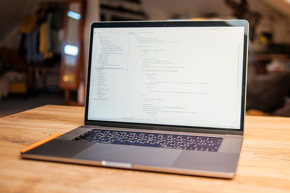 A modern laptop placed on a wooden table displaying lines of code on its screen, with a blurred background of a cozy indoor environment including a mirror, shelves with various items, and warm lightin